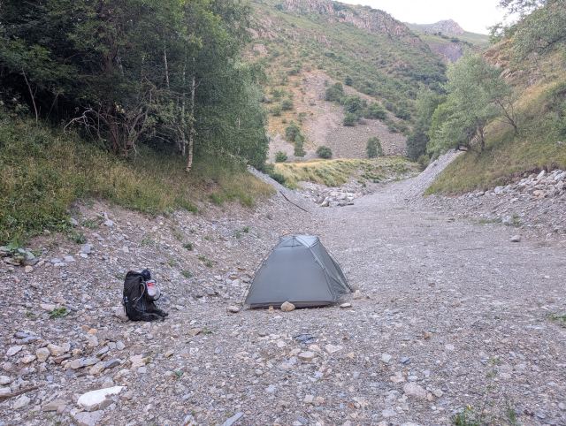 Teltplass på sandfyllingen ved siden av elven.